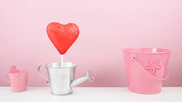 Il bastone di cuore di cioccolato sventato rosso con piccolo annaffiatoio d'argento e piccolo secchio rosa — Foto Stock