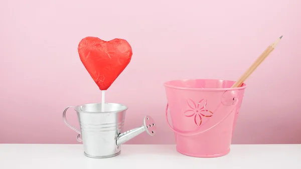 Il bastone di cuore di cioccolato sventato rosso con piccolo annaffiatoio d'argento e piccolo secchio rosa — Foto Stock