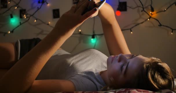 Jovem adolescente relaxante na cama com as mídias sociais no telefone inteligente móvel — Vídeo de Stock