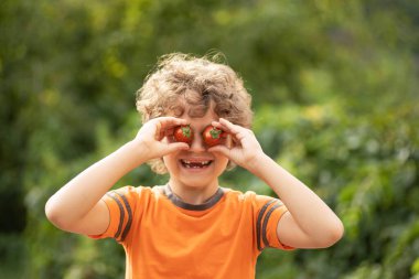 a boy with curly hair holds tomatoes in front of his eyes