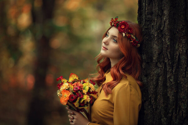 Red girl in the autumn forest on the head of the autumn wreath, in the hands of a bouquet. High quality photo