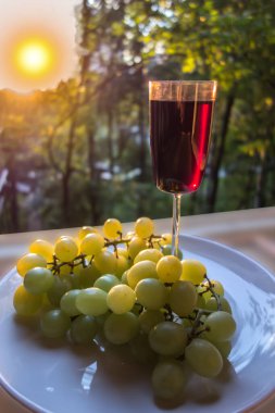 Gün batımında bir bardak kırmızı şarap ve bir demet beyaz üzüm..