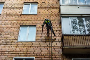 Temizlik servisinden bir endüstriyel tırmanıcı yüksek katlı bir konut binasının cephesini yıkıyor. Yüksek irtifada çalışan dağcı işçi. İp erişimi