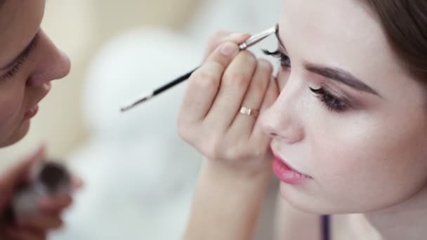 Makeup artist corrects the eyebrow line of model with the brush — Stock Video