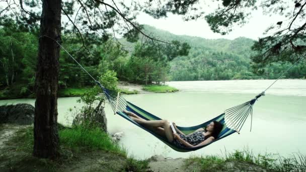 Woman relaxes reading book in hammock, swaying gently, in wood — Stock Video
