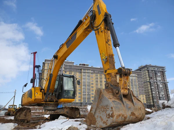 Bagger auf einer Baustelle vor einem mehrstöckigen Gebäude und blauem Himmel — Stockfoto