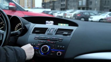 Bir adam bir radyo alıcısı ayarlar ve arabada ses düzeyini ayarlar