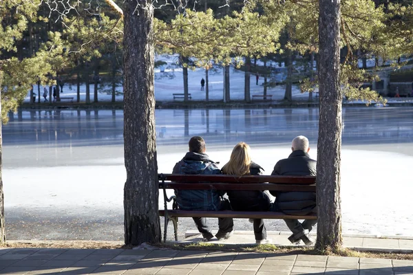 Tre personer sitter på en träbänk — Stockfoto