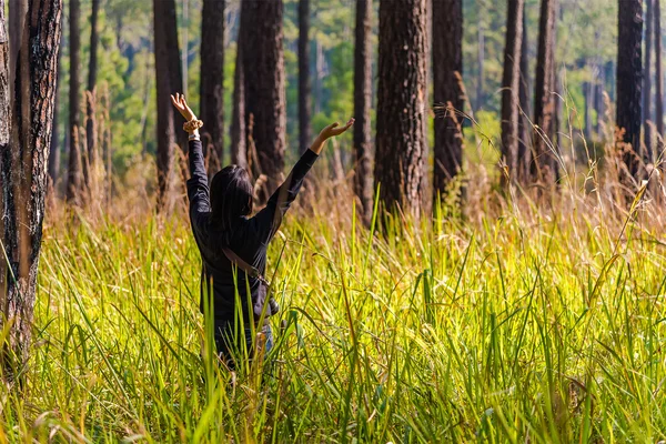 Mujer joven extendiendo la mano en el bosque verde alrededor del campo de hierba . — Foto de Stock