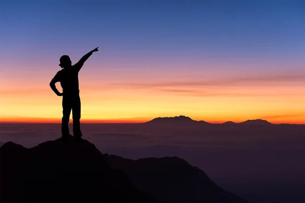 Dağ tepesinde duran ve gökyüzü için işaret eden kadın silüeti.