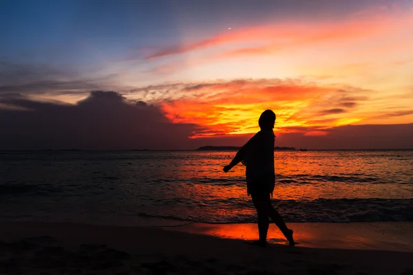 Σιλουέτα του νεαρή γυναίκα χαλαρώνοντας στην παραλία το ηλιοβασίλεμα. — Φωτογραφία Αρχείου