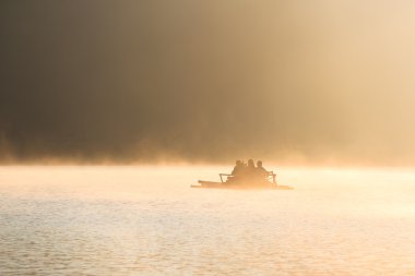 İnsanlar güneş doğarken bir gölde rafting bambu.