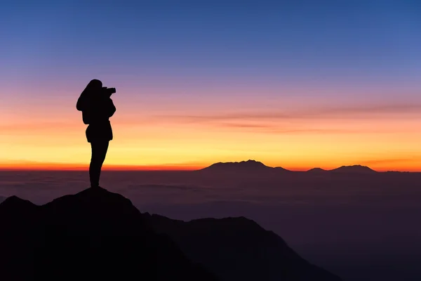 Силуэт женщины, фотографирующей на вершине горы и — стоковое фото