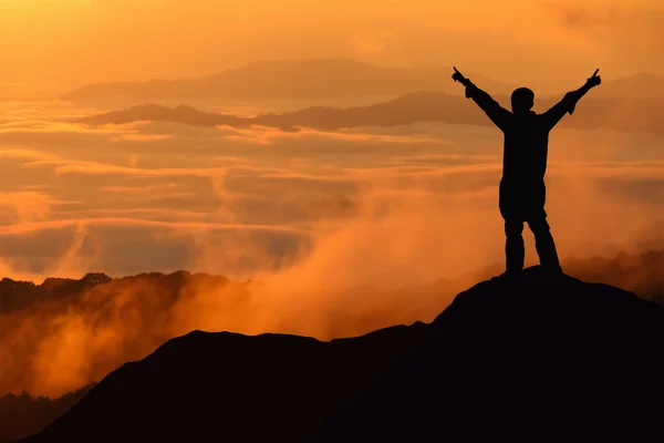 Silhouette di uomo turistico steso mano sulla cima di una montagna godere — Foto Stock