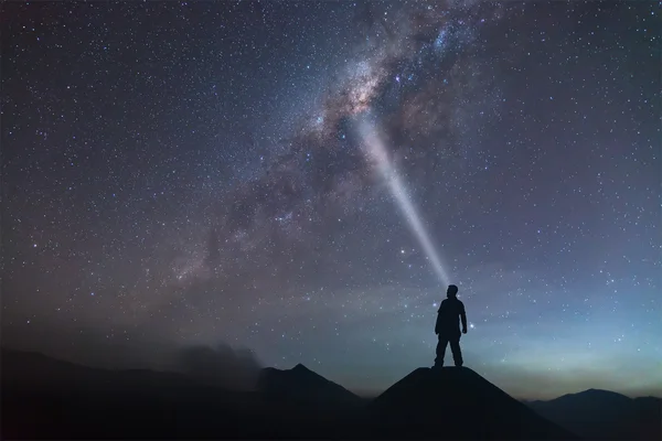 Mann steht auf Hügel und leuchtet zur Milchstraße. — Stockfoto