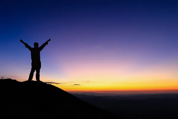 Die Silhouette des Menschen steht auf dem Gipfel des Berges und breitet die Hand aus, um den farbenfrohen Himmel des Sonnenuntergangs zu genießen. — Stockfoto
