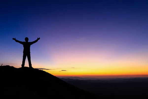 Silhouette dell'uomo in piedi e stesa mano sulla cima della montagna per godere del cielo colorato . — Foto Stock