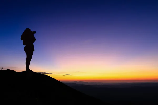 Σιλουέτα της γυναίκας λαμβάνοντας φωτογραφία στην κορυφή του βουνού και Απολαύστε πολύχρωμα ουρανό. — Φωτογραφία Αρχείου