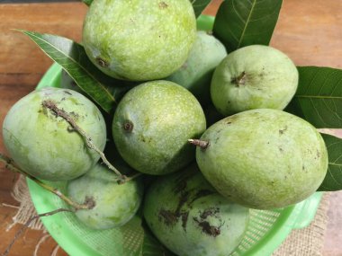 Fresh green mangoes with leaves arranged on burlap fabric, showcasing tropical fruit in a natural rustic setting.