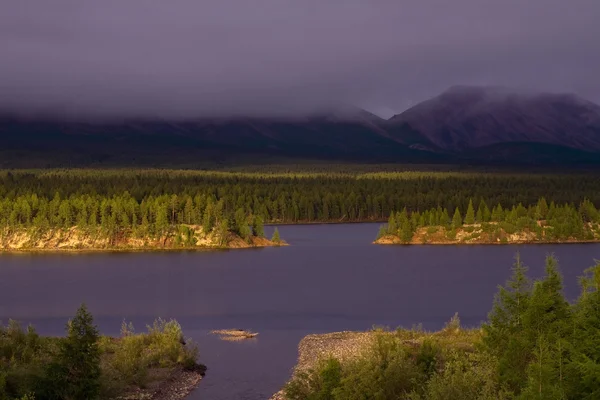 Lakeside in zonsondergang licht en lage wolken in de bergen. — Stockfoto