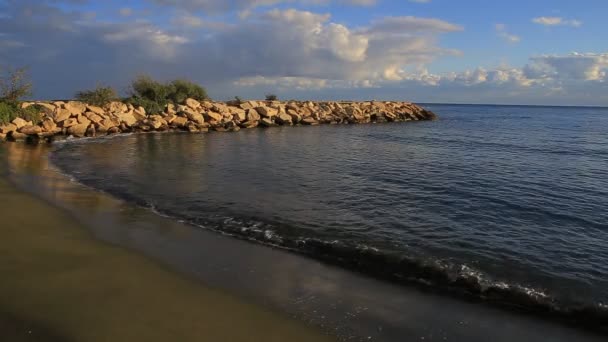 Ondas rodadas en una playa de arena y un muelle de piedra . — Vídeos de Stock