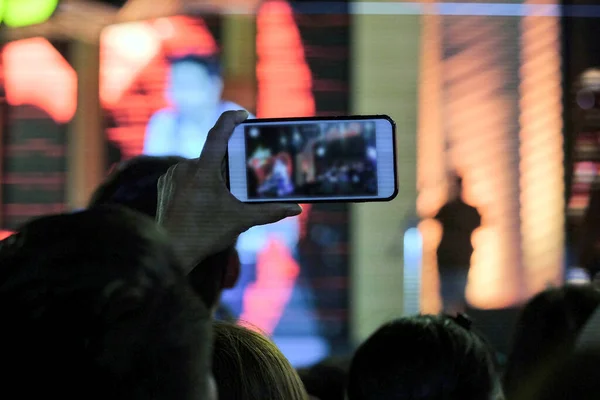 Tezahürat yapan kalabalık, gece açık havada mini-konser sahnesinde yer alan sanatçıları kaydetmek için akıllı telefon kullanıyor.