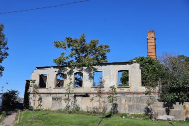 26-10-2025 İstanbul Türkiye: Kırık duvarları ve açık mavi gökyüzü altında tuğla bacası olan terk edilmiş fabrika binası