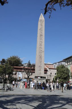 17-10-2025 İstanbul Türkiye: Sultanahmet Meydanı 'ndaki Theodosius Obelisk' i açık mavi gökyüzü altında ziyaret eden turistler