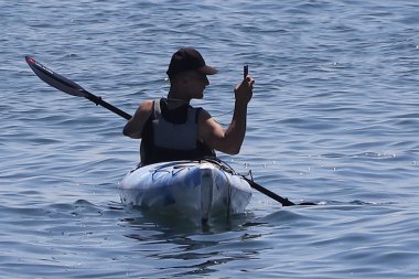 Siyah mayo giymiş, arka planda sırt çantası olan genç bir adam.