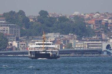 30-05-2024 İstanbul Türkiye: Arka planda yoğun kentsel ufuk çizgisi bulunan İstanbul Boğazı 'nda yolcu feribotu kalkıyor