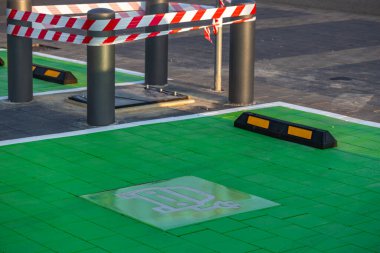 EV 'li elektrikli araçlar ve kaldırımda şarj sembolü olan yeşil boyalı bir park yeri. Sürdürülebilir ulaşım, eko hareketlilik ve modern şehir altyapısı kavramı.