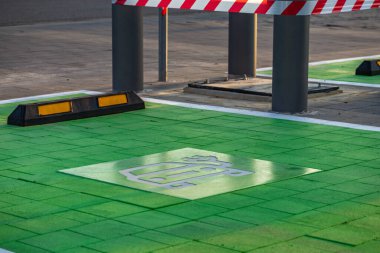 EV 'li elektrikli araçlar ve kaldırımda şarj sembolü olan yeşil boyalı bir park yeri. Sürdürülebilir ulaşım, eko hareketlilik ve modern şehir altyapısı kavramı.