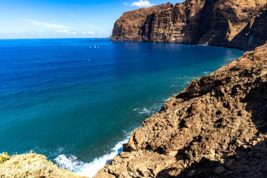 Stunning landscape of Los Gigantes cliffs on Tenerife, Canary Islands, with cactus growing on a rocky slope above the deep blue Atlantic Ocean under a partly cloudy sky. Travel, nature, and adventure concept.