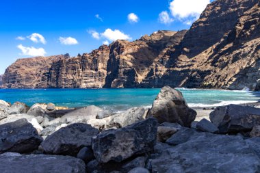 Stunning landscape of Los Gigantes cliffs on Tenerife, Canary Islands, with cactus growing on a rocky slope above the deep blue Atlantic Ocean under a partly cloudy sky. Travel, nature, and adventure concept.