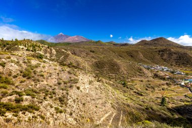 Beautiful view of Mount Teide volcano on Tenerife, Canary Islands, Spain. Majestic volcanic peak rising above green forests under a clear blue sky. Nature, travel, and adventure landscape concept.