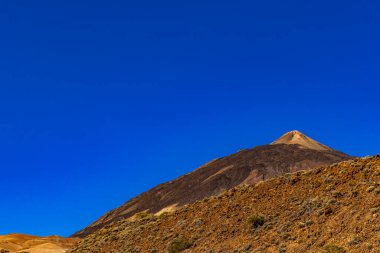 Beautiful view of Mount Teide volcano on Tenerife, Canary Islands, Spain. Majestic volcanic peak rising above green forests under a clear blue sky. Nature, travel, and adventure landscape concept.