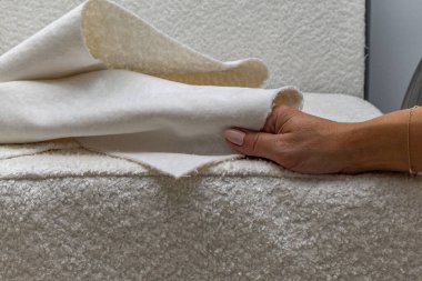 Close up of fitting a white boucl fabric cover on a corner sofa Concept of furniture renovation, upholstery work, and interior design craftsmanship.