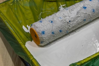 Yeşil plastik bir tepside duran beyaz boyaya batırılmış bir boya silindirini kapat. DIY ev yenileme, iç boyama araçları ve ekipman duvar dekorasyonu projesi için hazır.
