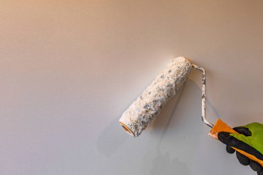 Bej bir duvarı boyarken, boya rulosunu tutan eldiven takmış bir eli kapat. DIY ev yenileme, dekorasyon ve fotokopi alanı ve doğal aydınlatma ile iç geliştirme kavramı