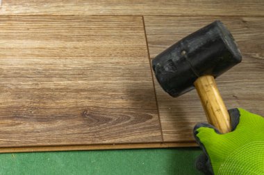 Döşeme kurulumu sırasında tahta lamine panelleri takmak için plastik çekiç kullanan yeşil koruyucu eldivenler takan işçilerin fotoğraflarını çek. DIY yenileme, hassas çalışma ve ev geliştirme danışmanı