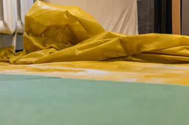 Kaplama veya vinil döşeme tesisatı için hazırlık aşamasındayız. Yeşil koruyucu eldivenlerle çalışan işçilerin elini kapat. Sarı buhar bariyerindeki kullanışlı bir bıçakla yeşil zemin kaplamasını kes.. 