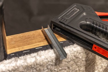 Siyah döşeme zımbası ve yumuşak beyaz kumaşla kaplı ahşap bir çerçeveye yerleştirilmiş metal zımba. Mobilya yenileme, döşeme ve ev geliştirme araçları kavramı