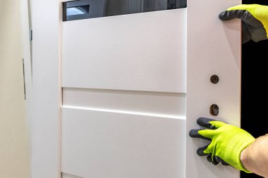Beyaz ahşap kapı için kilidi olan siyah bir kapı kolu takmak, çerçevedeki kapıyı çerçevelemek, iç kapılar takılırken eldivenlerle çalışmak