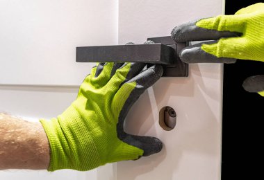 Beyaz ahşap kapı için kilidi olan siyah bir kapı kolu takmak, çerçevedeki kapıyı çerçevelemek, iç kapılar takılırken eldivenlerle çalışmak