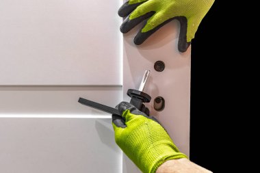 Beyaz ahşap kapı için kilidi olan siyah bir kapı kolu takmak, çerçevedeki kapıyı çerçevelemek, iç kapılar takılırken eldivenlerle çalışmak