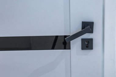 Siyah bir kapı kolu, kangurunun beyaz ahşap kapısına monte edilmiş.