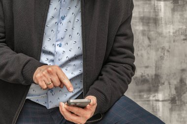 Uzun kollu mavi gömlekli ve şık pantolonlu bir adam hanında cep telefonu olan beton bir duvarın karşısında duruyor.