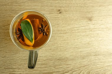 Temiz, çift duvarlı bir bardak sıcak çayla dolu doğu baharatları, tarçın çubukları, ambar, karanfil, portakal, yıldız anason, ahşap bir masada sıcak bir içecek.