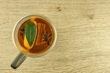 Temiz, çift duvarlı bir bardak sıcak çayla dolu doğu baharatları, tarçın çubukları, ambar, karanfil, portakal, yıldız anason, ahşap bir masada sıcak bir içecek.