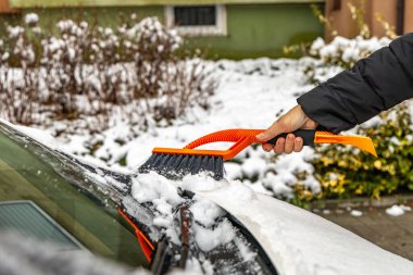 Bir kadın işe gitmeden önce arabasından kar temizliyor, turuncu yumuşak fırçalı bir arabadan kar temizliyor, kışın araba sürmek için bir araba hazırlıyor, bir arabanın gövdesinden karı kaldırıyor, küreksiz bir araç için bir bilet.